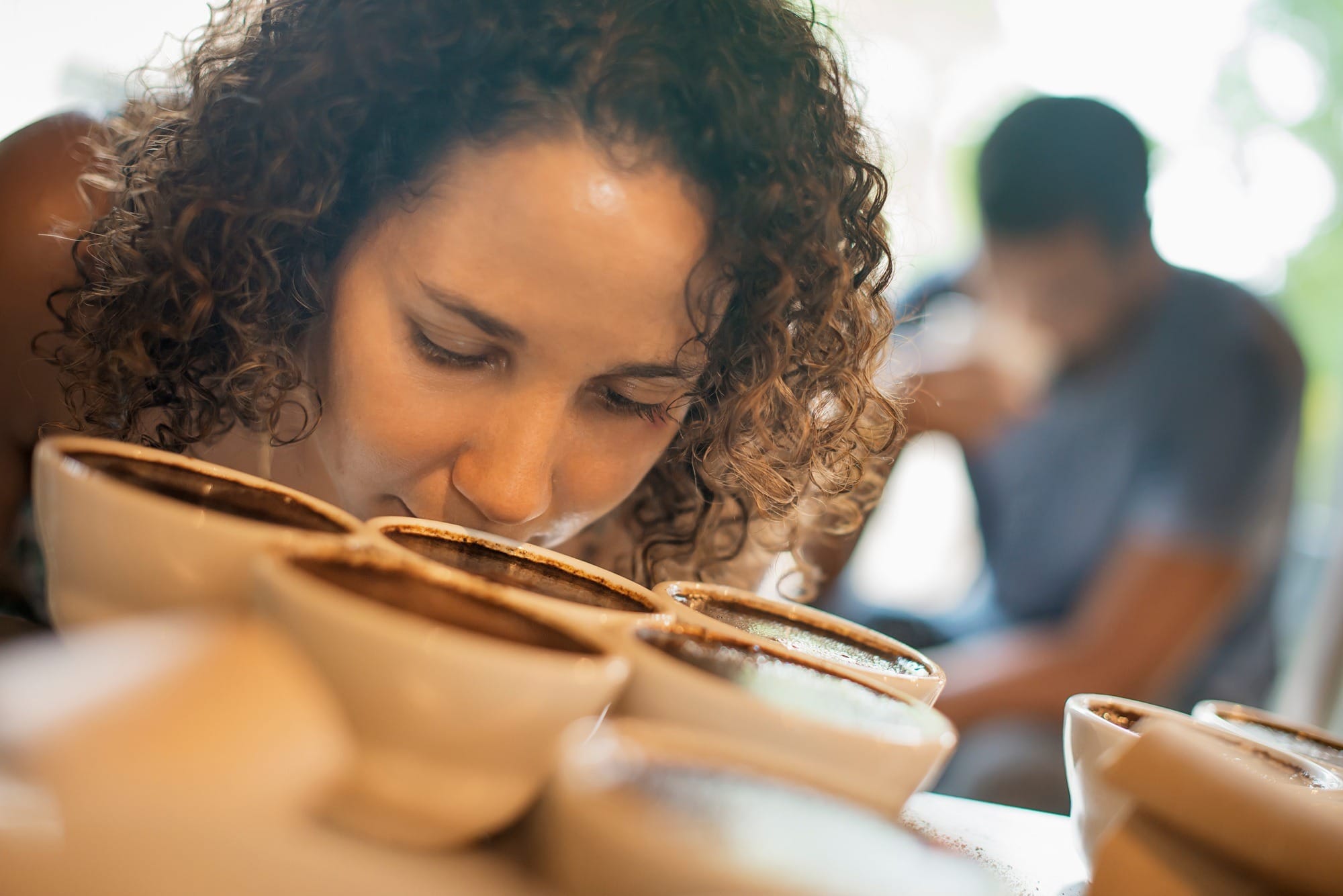 A woman smelling coffee samples in a coffee processing shed.