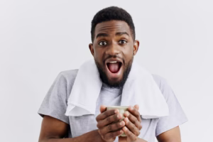 African american man holding coffee cup with surprised expression on white background, capturing