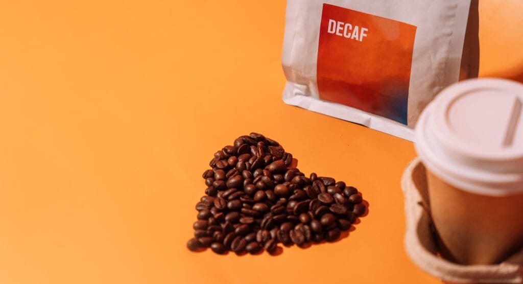 coffee-beans-in-the-shape-of-a-heart-on-an-orange-background-next-to-packaging-with-text-decaf-and-a-1024x556 Café Tem Calorias? A Verdade Definitiva Sobre o Cafezinho e a Balança