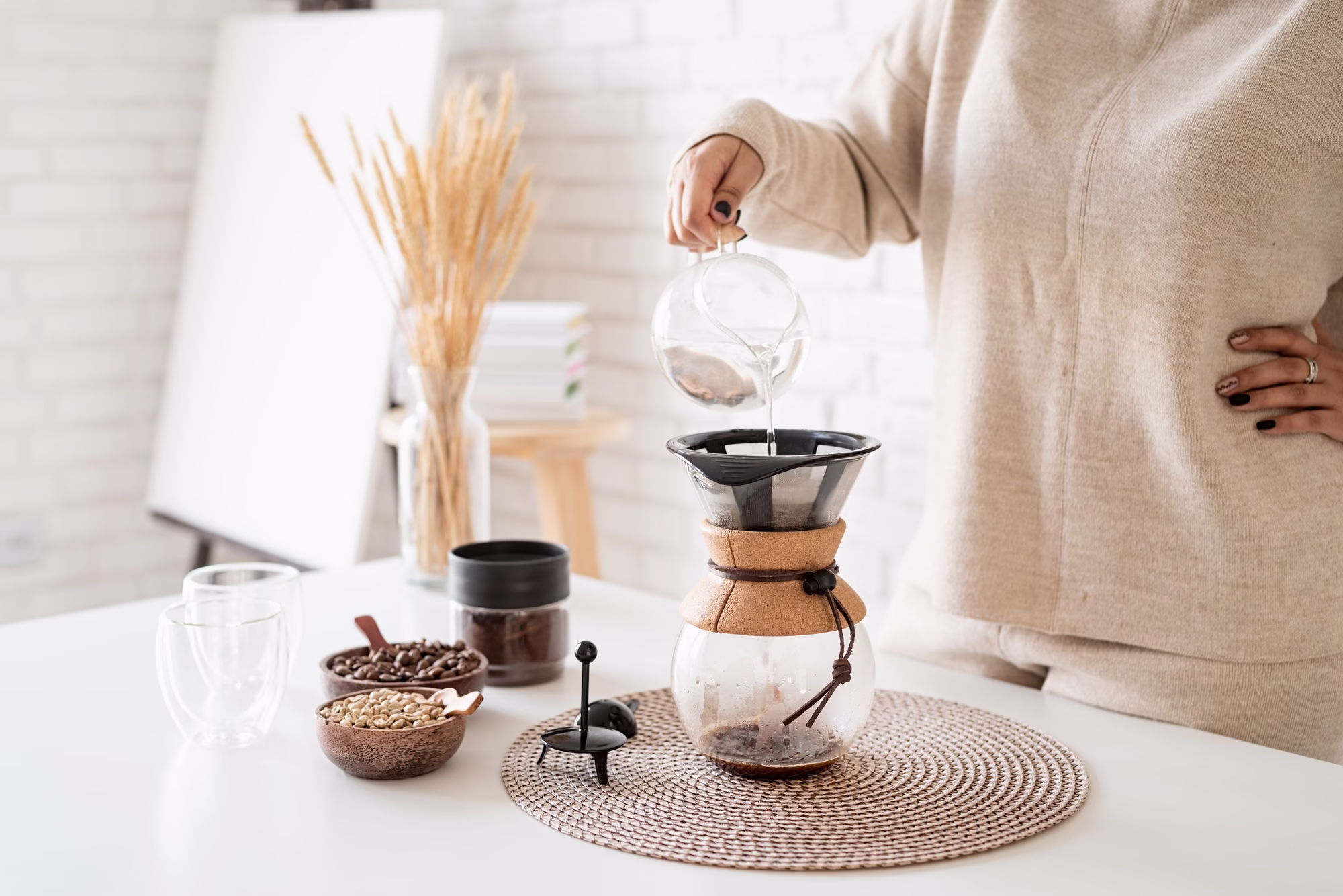 Young woman brewing coffee in chemex, pouring hot water into the filter